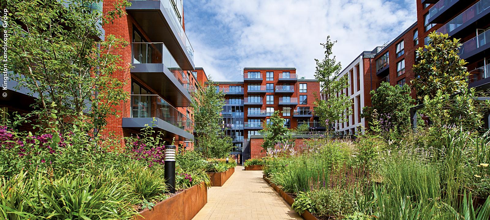 Courtyard with blooming plant beds and a pathway surrounded by residential buildings