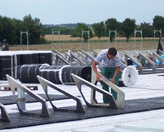 The solar base plates SB 200, each of which has a solar base frame SGR 35/90 for mounting the modules, are installed over the drainage channels Fixodrain® XD 20 (rolls), which are fitted across the entire area. Man installs solar base frames on a green roof