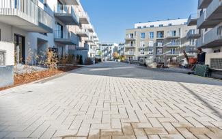 Next to the finished green areas and surfaces, the works on the right-hand side of the courtyard are still in full swing. © Strassen- und Tiefbau Urban GmbH Newly installed green areas and walkways within a residential complex.