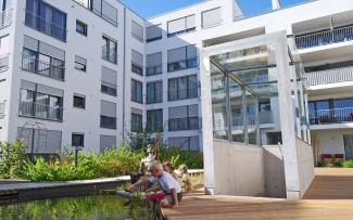 Children sitting at a pond in front of the staircase leading to the underground car park